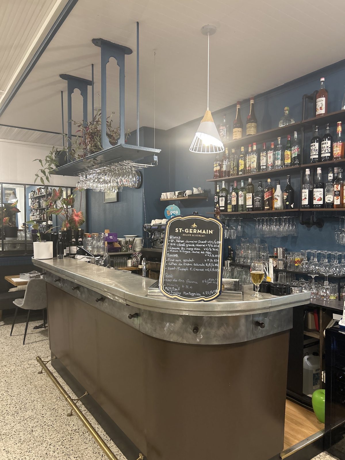 Le comptoir en zinc, l'ardoise des vins et les étagères de bouteilles sur le mur bleu