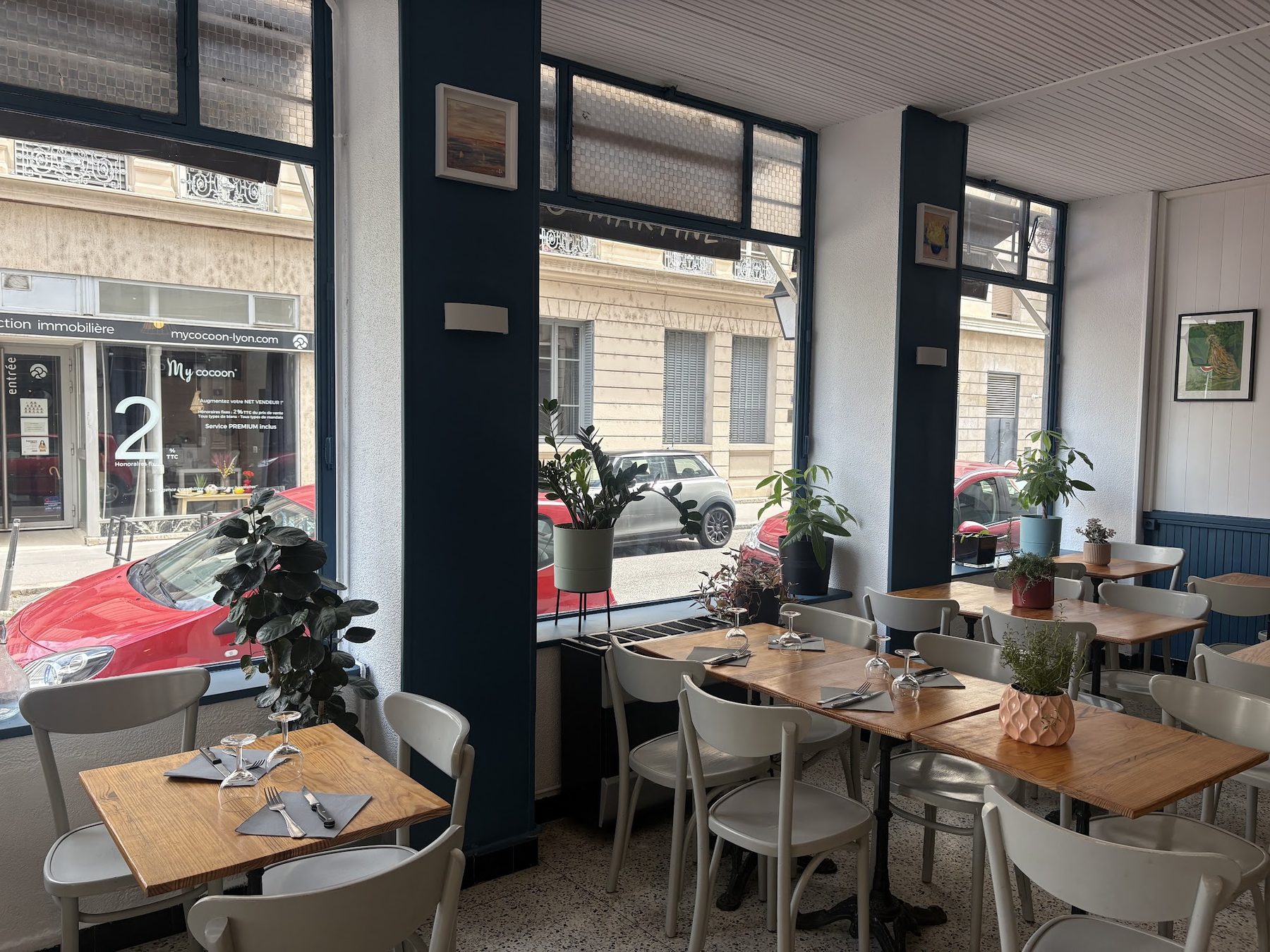 La salle du Café de la Mairie : tables en bois, grandes baies bleu marine, plantes
